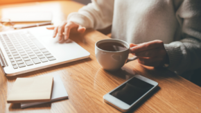 A person holding a cup of coffee while working on a laptop, symbolizing focus and planning during life's transitions like divorce.