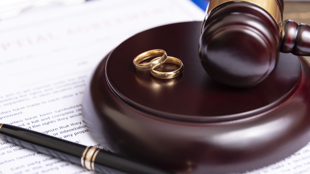 Golden wedding rings on a judge's gavel with legal documents in the background.