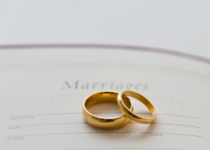 Two gold wedding rings placed on a marriage certificate with "Marriages" written at the top.